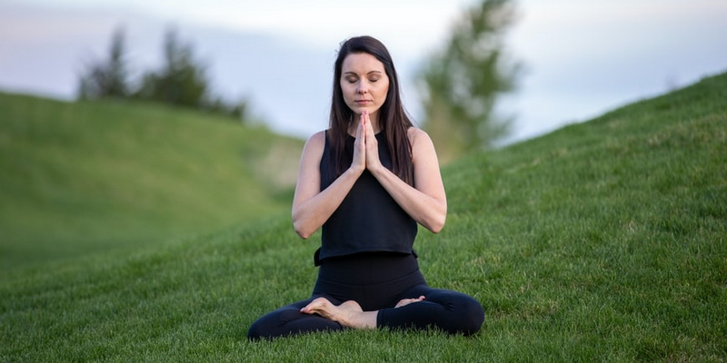 La fille est assise sur l'herbe, les mains croisées.